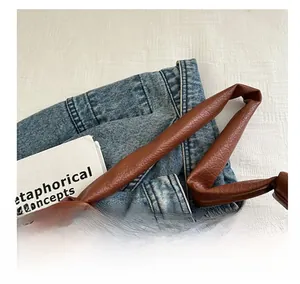 Detail of blue denim shoulder bag with brown lychee leather strap and knot design