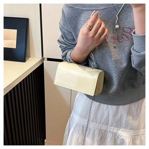 Detail of a creamy beige mini bag with silver metal handle and embossed mim logo