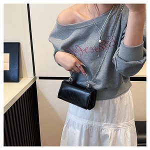Close-up of black leather crossbody bag with metal chain strap and logo on a model