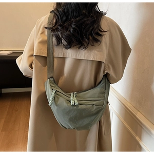 Detail of green crescent nylon crossbody bag with woven rope zippers on beige trench coat