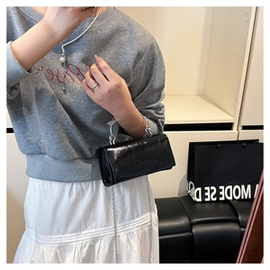 Detail of a black patent leather mini handbag with silver metal ring handle and chain