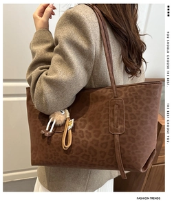 Model view of a large brown leopard print tote bag with a plush doll charm accessory