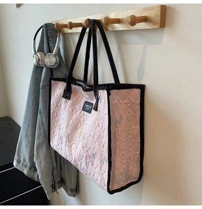 Close-up of pink quilted tote bag with colorful embroidery and black leather trim