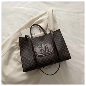 Detail of caramel tote bag with M-monogram pattern and embossed logo on beige blazer