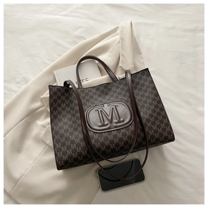 Close-up of dark brown tote bag featuring M-letter monogram pattern and embossed leather logo