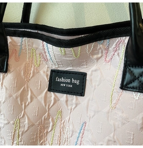 Detail of pink quilted tote bag with multi-color wave embroidery and leather patch logo