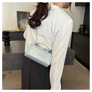 Close-up of a light blue glossy mini bag with a silver handle and chain strap on a model