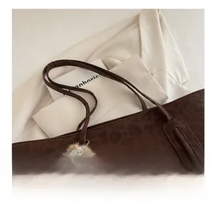 Close-up of brown leopard print tote bag with a soft plush pom-pom charm and dual straps