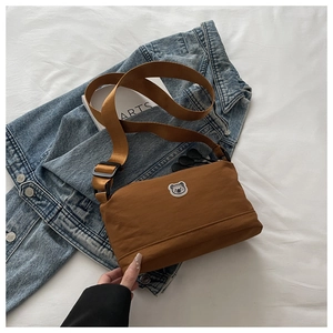 Detailed top view of a brown nylon crossbody bag with cute bear patch on white fabric