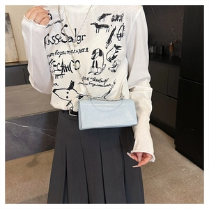Detail of light blue glossy chain bag with metal handle worn by model in casual setting