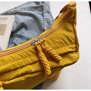 Detailed close-up of yellow nylon crossbody bag with dual-zipper and woven puller cords