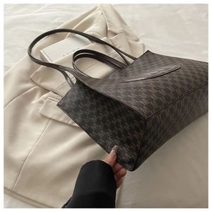 Macro detail of the brown tote bag featuring M-pattern monogram and oval leather patch