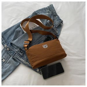 Flat lay of a brown canvas crossbody bag with a bear logo on a blue denim jacket