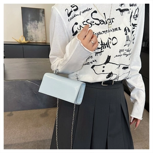 Detail of light blue patent leather mini bag with silver chain strap on model