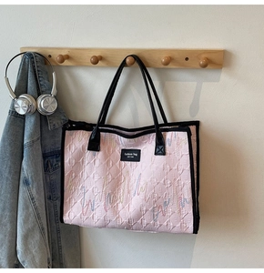 Detail of pink quilted tote bag featuring multi-colored wavy embroidery and leather label