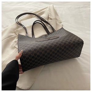 Detail of coffee tote bag featuring monogram pattern and leather patch on white bedding