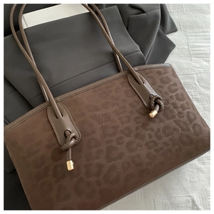 Detail of a leopard print brown tote bag with slim shoulder straps and gold metal tips