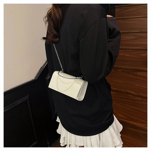 Close-up of white leather crossbody bag with silver chain strap and metal handle