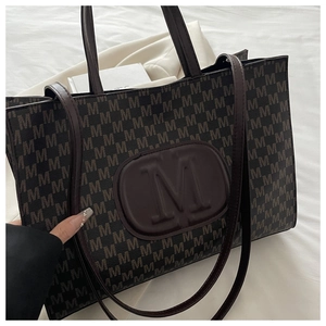 Macro detail of large embossed M logo and monogram pattern on dark brown tote bag