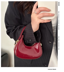 Detail of a deep red crescent hobo bag in glossy patent leather with gold-tone hardware