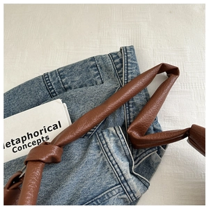 Detail of a brown leather shoulder bag featuring a knotted strap and litchi texture finish
