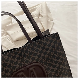 Detailed view of tote bag featuring monogram pattern and large embossed letter M logo