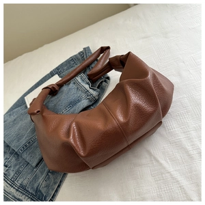 Close-up of brown pleated shoulder bag with knotted handle detail on casual background
