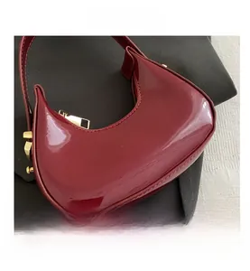 Detail of dark red crescent hobo bag in glossy patent leather with gold hardware