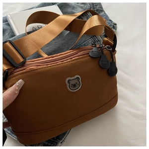 Detail of tan nylon crossbody bag featuring adjustable strap and cartoon bear accents