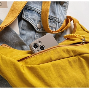 Detail of yellow nylon crossbody bag on denim jacket showing zipper and phone storage