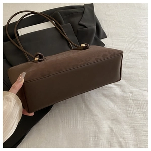 Detail of dark brown suede tote bag with knotted shoulder strap on minimalist background