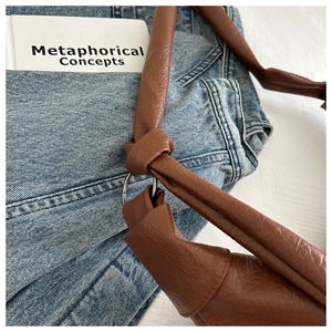 Detail of dark brown leather shoulder bag with lychee texture and knotted strap design