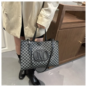 Detail of trendy monogram tote bag showing textured M patterns and 3D black logo plate