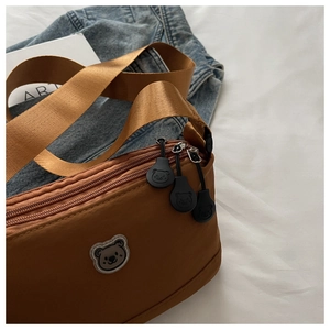 Detail of a brown nylon crossbody bag featuring cute cartoon bear patches and zippers