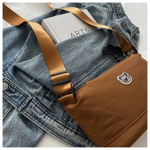 Close-up of brown nylon crossbody bag with cute bear emblem on denim jacket background