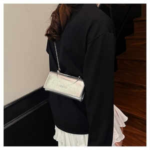 Close-up of silver metallic chain bag with mim logo worn by a model on a staircase