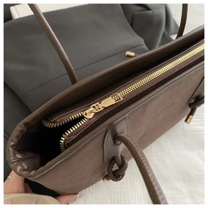 Close-up of golden zipper and knotted shoulder strap on brown suede tote bag