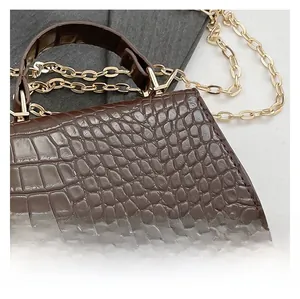 Detail shot of a dark brown crocodile texture handbag with gold metal chain strap