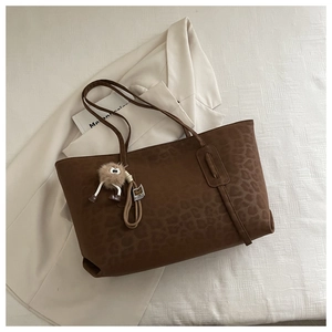 Detail of leopard print tote bag with plush charm on a cream blazer background