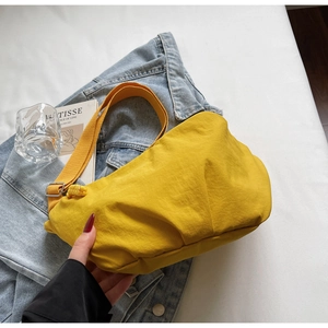 Detail of yellow nylon pleated dumpling bag with adjustable strap on denim background