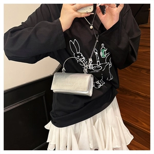 Detail of silver metallic square handbag with metal handle and chain strap on a model