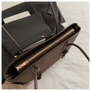 Detail of dark brown tote bag with gold zipper hardware and knotted rope handle
