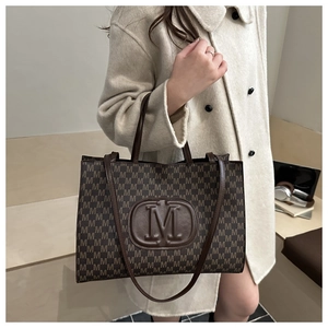 Detailed view of brown tote bag with all-over M-letter print and top handles on model