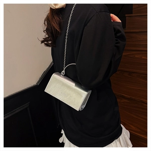 Close-up of silver metallic chain bag with embossed logo on white pleated skirt background