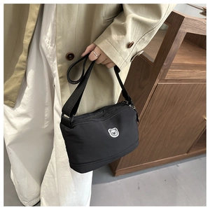 Detail of black crossbody bag with bear patch and multi-zipper compartments on fabric