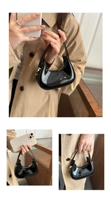 Detail of glossy black patent leather crescent bag with gold zipper and minimalist shape