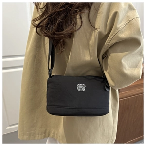 Close-up of black nylon crossbody bag with a cute bear patch on a beige trench coat