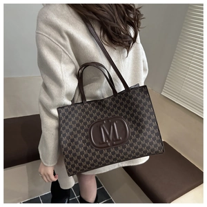 Detail of dark coffee tote bag featuring M-letter jacquard texture and logo emblem