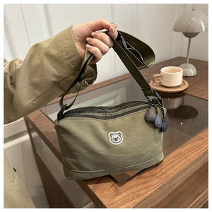 Detailed close-up of olive green nylon crossbody bag with cute bear logo and strap