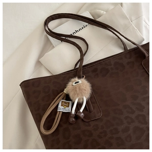 Detail of leopard print tote bag with a whimsical fuzzy monster charm attachment